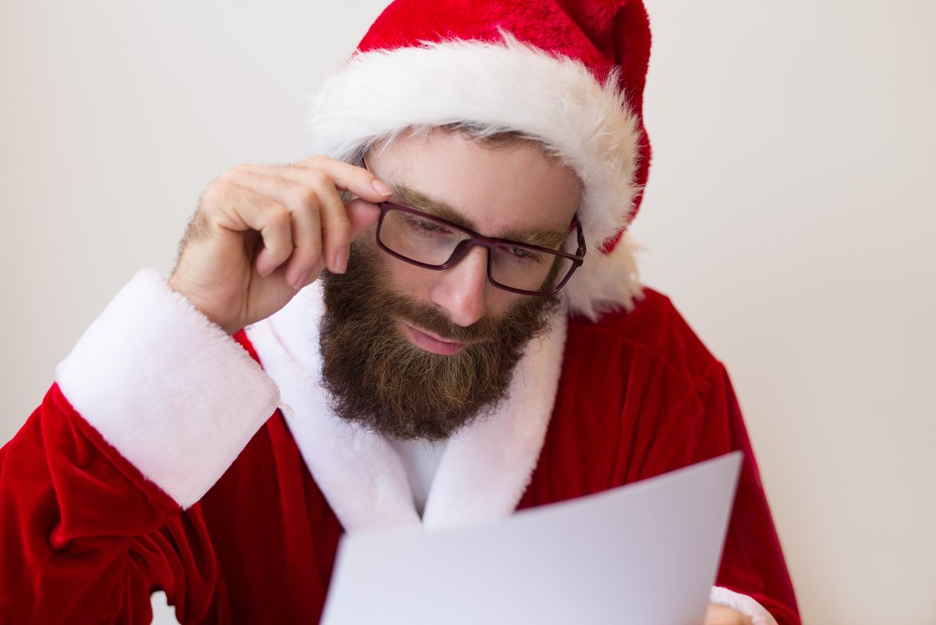 Focused guy wearing Santa costume and reading document. Bearded man working. Christmas and business concept. Front view.